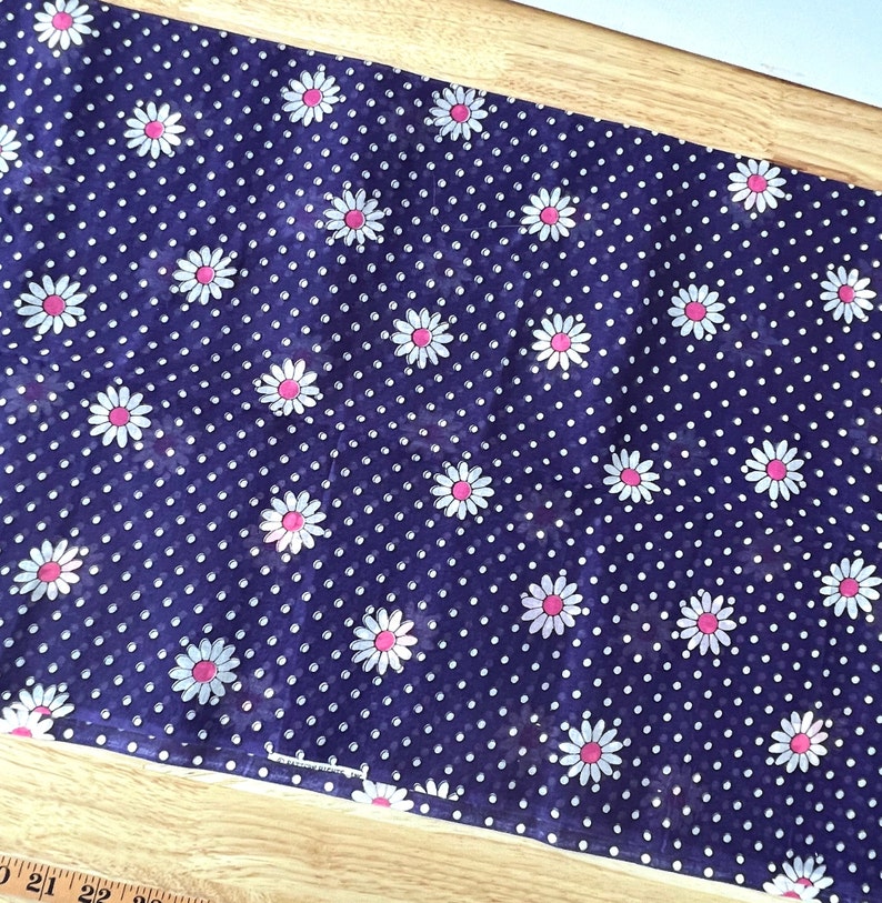 Peut inclure: Un tissu bleu fonc&eacute; avec un motif r&eacute;p&eacute;t&eacute; de marguerites blanches &agrave; centres roses et de petits pois blancs. Le tissu est probablement en coton ou dans une mati&egrave;re similaire, adapt&eacute; aux projets de couture ou de d&eacute;coration int&eacute;rieure.