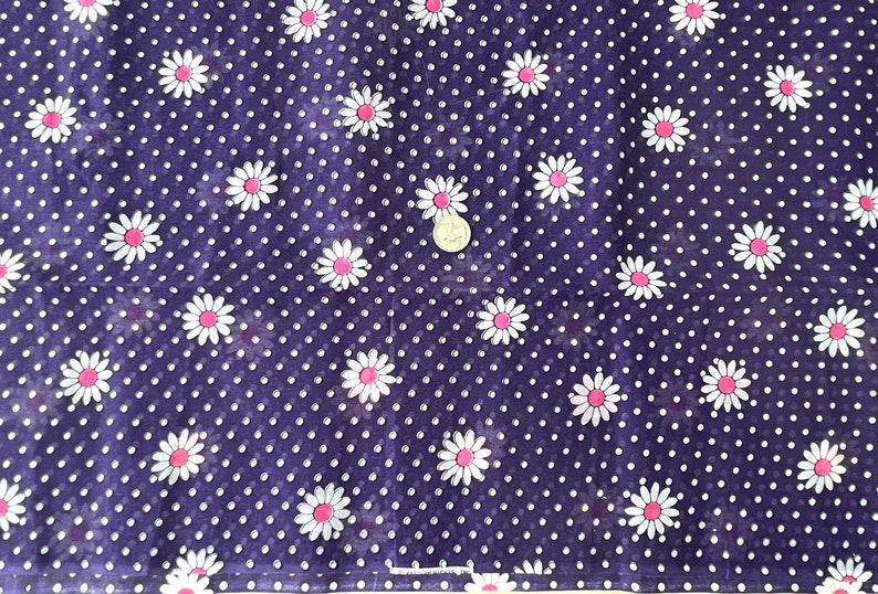 Peut inclure: Gros plan sur un tissu bleu fonc&eacute; orn&eacute; de pois blancs et de motifs de fleurs de marguerite. Les marguerites ont des p&eacute;tales blancs et des centres roses. Id&eacute;al pour les v&ecirc;tements ou les travaux manuels.
