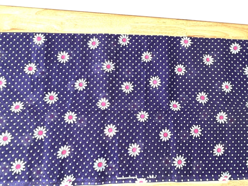 Peut inclure: Un tissu bleu marine avec un motif de pois blancs et des marguerites blanches &agrave; c&oelig;ur rose. Le tissu rectangulaire pourrait &ecirc;tre un chemin de table ou un tissu d&eacute;coratif.