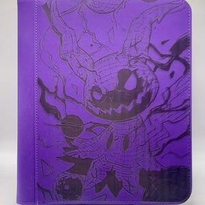 May include: A purple trading card binder featuring a dark illustration of a creature with a pumpkin-like head and tree-like features. The binder is a solid purple color with a stitched spine and a dark purple graphic on the front.
