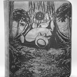 May include: Gray binder with a detailed forest scene featuring a sleeping cartoon character. The artwork is etched into the cover, with trees, foliage, and a path. The binder has a solid gray spine.