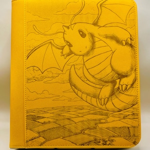 May include: A yellow trading card binder featuring a detailed illustration of a dragon. The dragon is depicted in a sketched style, with a landscape background. The binder has a stitched border.