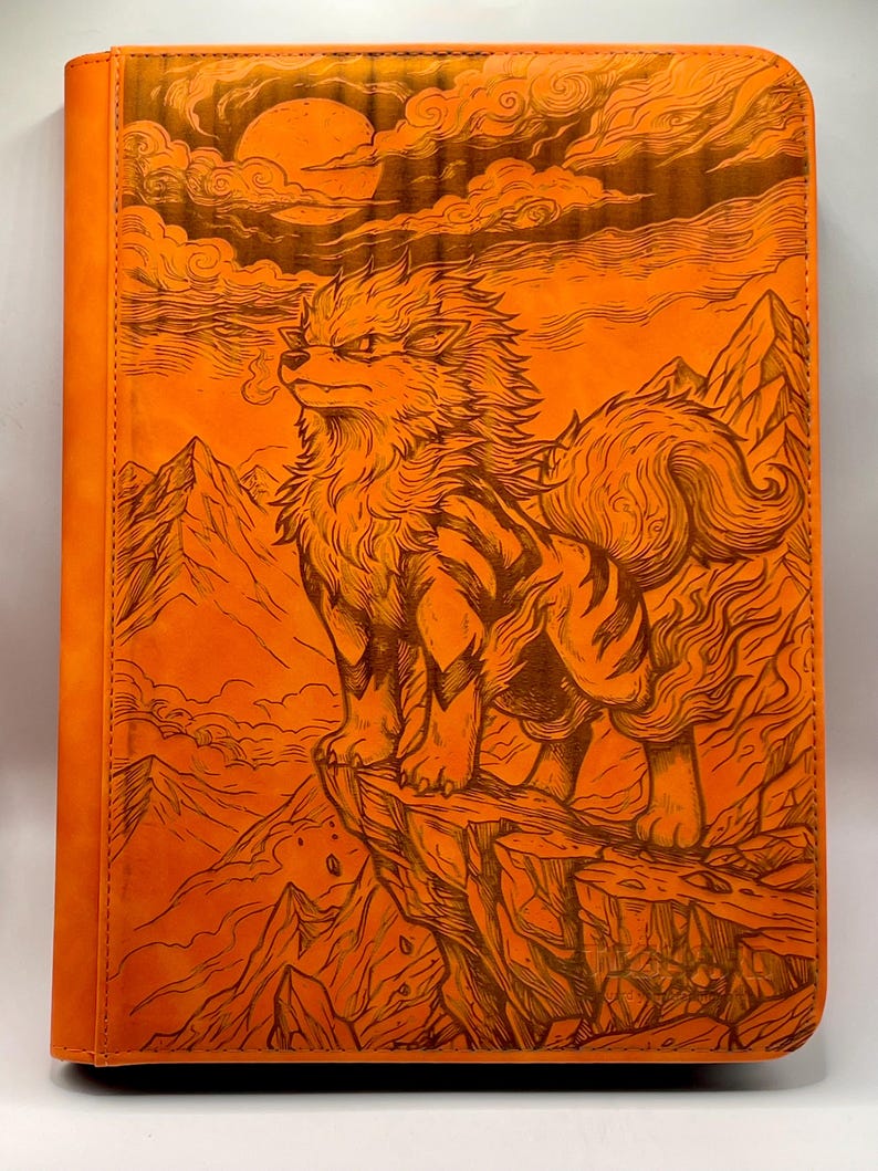 May include: Orange leather journal featuring a detailed illustration of a canine-like creature standing on a cliff, with a mountain range and a sun in the background. The artwork is in a detailed, line-art style.