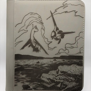May include: A light gray rectangular trading card binder featuring a dark laser-engraved illustration of two flying creatures above a body of water with rocky shores. The cover has a textured surface and a small logo in the bottom right corner.