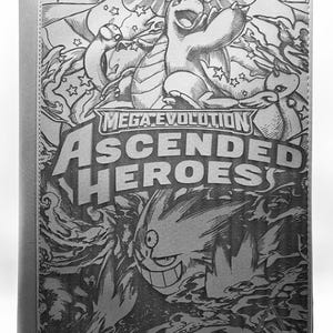 May include: A gray card binder featuring a detailed black and white illustration of various characters and the text "MEGA EVOLUTION ASCENDED HEROES". The binder has a solid gray spine and is held open by a metal stand.