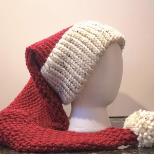 May include: A handmade Santa hat, featuring a deep red knit body and a white knit brim. The hat has a long, pointed shape with a white pom-pom at the end. The hat is displayed on a white mannequin head.