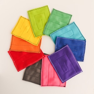 May include: A set of nine felt squares in a rainbow color pattern. Each square has a stitched border and a small opening in the center.