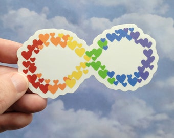 May include: A rainbow infinity symbol sticker made of small hearts. The sticker is on a white background and is being held by a hand.