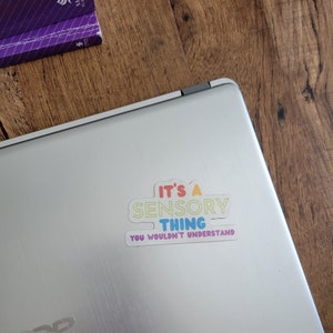 May include: A white laptop with a colorful sticker that reads "It's a Sensory Thing You Wouldn't Understand".
