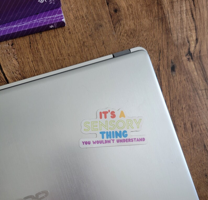 May include: A white laptop with a colorful sticker that reads "It's a Sensory Thing You Wouldn't Understand".