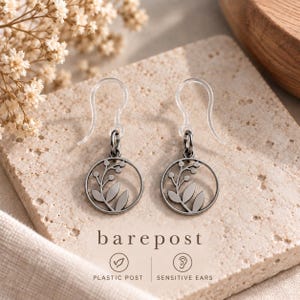 May include: A pair of earrings featuring dark gray circular charms with a cutout botanical leaf and berry design. The earrings have clear plastic hook posts. The text "barepost" is printed below the earrings, along with "PLASTIC POST" and "SENSITIVE EARS".