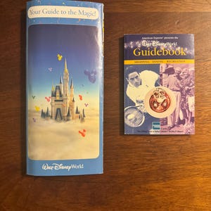 K&ouml;nnte beinhalten: Zwei Vintage-Reisef&uuml;hrer von Walt Disney World. Einer ist eine blaue Brosch&uuml;re mit einer Schlossillustration und dem Text "Your Guide to the Magic!". Der andere ist ein Reisef&uuml;hrer mit dem Text "Guidebook" und "American Express presents the Walt Disney World".