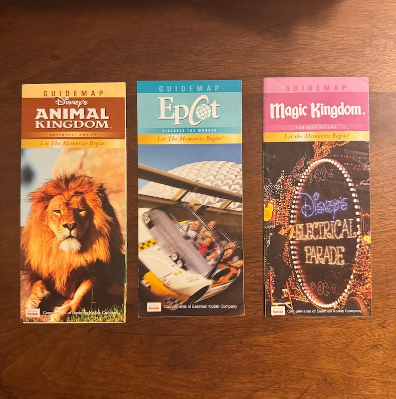 K&ouml;nnte beinhalten: Drei Vintage-F&uuml;hrerpl&auml;ne von Disney World. Die Karten sind f&uuml;r Animal Kingdom, Epcot und Magic Kingdom. Jede Karte zeigt farbenfrohe Grafiken und Text, einschlie&szlig;lich der Parknamen und "Let the Memories Begin!"