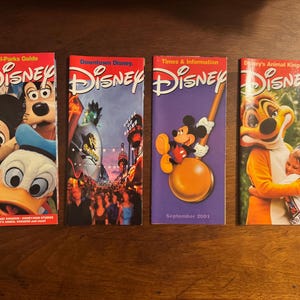 K&ouml;nnte beinhalten: Vier Disney-Parkf&uuml;hrer. Die Cover zeigen Micky Maus, Goofy, Donald Duck und Szenen aus den Parks. Ein F&uuml;hrer ist lila mit Micky Maus und dem Text "September 2001."