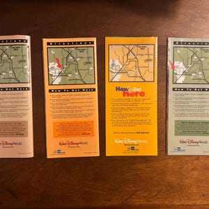 K&ouml;nnte beinhalten: Vier gefaltete Papierkarten mit den Texten "Directions" und "How to Get Here" werden angezeigt. Die Karten zeigen eine Karte der Region Orlando und sind in den Farbt&ouml;nen Beige, Orange und Gelb gehalten. Die Karten sind f&uuml;r Walt Disney World.