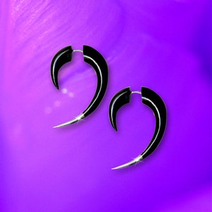 May include: A pair of black horn-shaped earrings with silver accents. The earrings are curved and have a pointed tip.