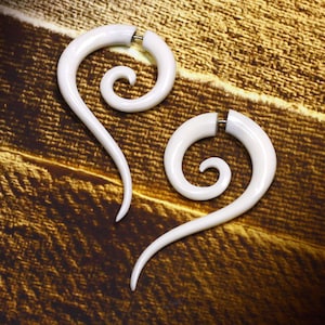 May include: Two white spiral ear gauges, made of wood, with a smooth finish. The gauges are in the shape of a spiral and are designed to be worn in stretched earlobes.