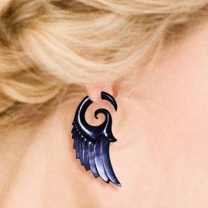 K&ouml;nnte beinhalten: Ein schwarzer Fl&uuml;gel-Ohrring mit einem Spiraldesign. Der Ohrring ist aus einem dunklen, polierten Material gefertigt.