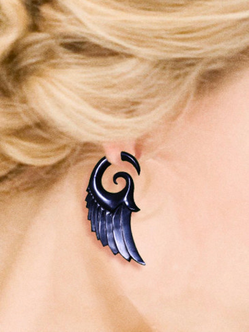 K&ouml;nnte beinhalten: Ein schwarzer Fl&uuml;gel-Ohrring mit einem Spiraldesign. Der Ohrring ist aus einem dunklen, polierten Material gefertigt.
