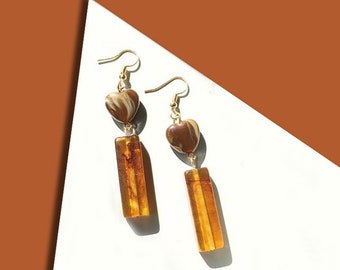 May include: A pair of gold dangle earrings with brown and white heart-shaped beads and long rectangular brown beads.