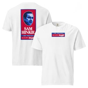 May include: A white t-shirt featuring a graphic design on the front and back. The back displays a portrait of Sam Hinkie above the text "SAM HINKIE", "THE PROCESS", and "July 14, 2013 - ???". The front chest area shows a smaller version of the same text.