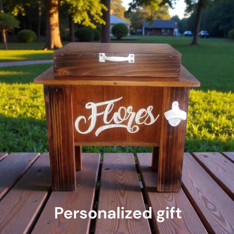 May include: A wooden cooler with a dark stain, featuring the name "Flores" in white script. It has a matching lid with a white handle and a bottle opener. The text "Personalized gift" is at the bottom.