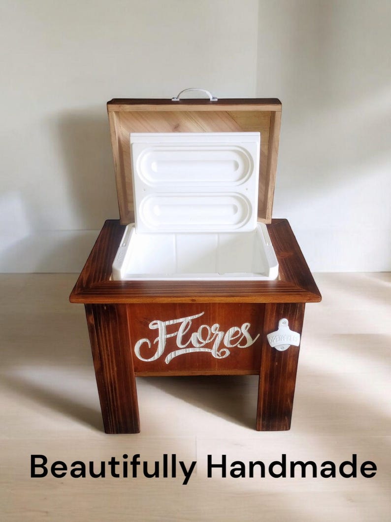 May include: A wooden cooler with a hinged lid and a white interior. The cooler is stained a dark brown and features the word "Flores" in white script. A bottle opener is attached to the side. The text "Beautifully Handmade" is at the bottom.