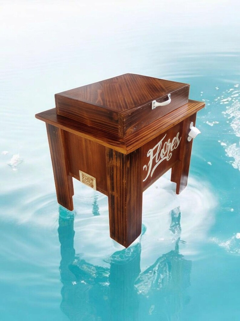 May include: A wooden cooler with a dark brown finish, featuring a rectangular box on top and a lower compartment with the word "Flores" in white script. It has a white bottle opener and a small handle on the box.