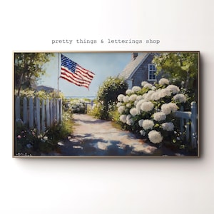 May include: A framed painting of a coastal scene with a waving American flag. A white picket fence and lush white hydrangeas line a path leading to a gray-shingled house. The text "pretty things & letterings shop" is at the top.
