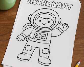 May include: Black and white line drawing of an astronaut on a stack of white paper. The word "ASTRONAUT" is printed at the top. A green mug of coffee and a set of colored pencils are on the wooden surface.