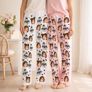 May include: Two pairs of pajama pants, one white and one pink, each featuring a repeating pattern of a child's face, a crown, and the text "BEST MOM EVER". The pants have a drawstring waist.