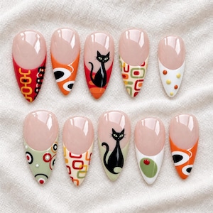 Pode incluir: Um conjunto de dez unhas postiças em formato amendoado com base nude e vários designs nas pontas, incluindo silhuetas de gatos pretos, padrões geométricos laranja e vermelhos, círculos verdes e pontos multicoloridos em fundos brancos e verde-sálvia.