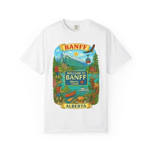 May include: White t-shirt featuring a colorful graphic of Banff, Alberta, Canada. The design includes mountains, a lake, a cable car, and the text "BANFF" and "WELCOME TO BANFF Alberta Canada".