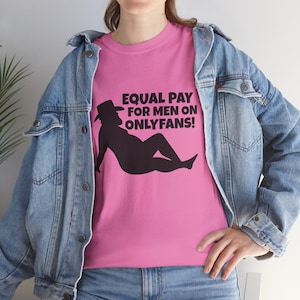 Puede incluir: Camiseta rosa con el texto "EQUAL PAY FOR MEN ON ONLYFANS!" y una silueta negra de una persona con sombrero de vaquero. La persona está reclinada. La modelo lleva una chaqueta vaquera azul.