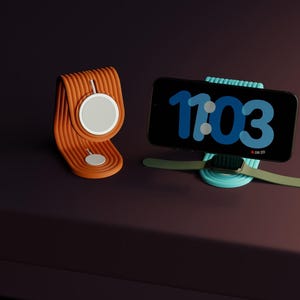 以下が含まれることがあります： オレンジと白のワイヤレス充電器スタンドと、11:03の時刻を表示する黒いスマートフォン。電話は、緑色の時計バンドが付いた水色のスタンドにあります。充電器は濃い茶色の表面にあります。