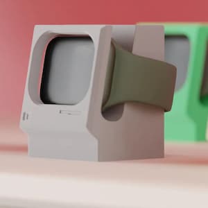 May include: A white Apple Watch charging stand in a retro computer design. The stand has a grey screen area and a green watch strap. Other stands in green and yellow are visible in the background.