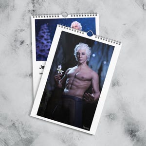 Puede incluir: Dos calendarios encuadernados en espiral. El calendario frontal presenta a una persona con cabello blanco sosteniendo una flor blanca. El fondo es un entorno oscuro similar a una cueva. El segundo calendario muestra una imagen similar.