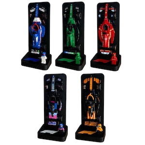 Peut inclure: Cinq modèles réduits de voitures de course de différentes couleurs, dont le bleu, le vert et le rouge, exposés sur des présentoirs noirs. Chaque modèle a un design unique et est accompagné d'une petite figurine. Les présentoirs ont une base et un panneau arrière.
