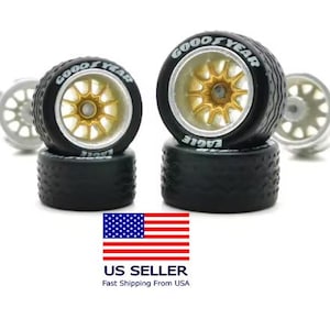 May include: Set of four model car wheels. The tires are black with "Goodyear" and "Eagle" branding in white. The rims are gold-colored with a starburst design. Two additional silver wheels are in the background.
