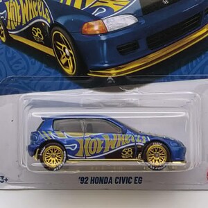 May include: A blue and gold Hot Wheels die-cast car of a '92 Honda Civic EG. The car has gold wheels and accents, with the Hot Wheels logo and other graphics. The packaging is blue with the Hot Wheels logo and the text "HDH54".