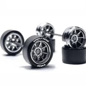 May include: A set of miniature scale model car wheels and tires featuring silver multi-spoke rims and black rubber tires. The front-most tire displays white Goodyear Eagle lettering on the sidewall. The components are connected by thin metal axles.