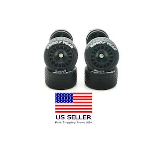 May include: Set of four black Goodyear tires with white lettering. The tires are stacked in pairs, with the Goodyear logo visible on the sidewalls. The wheels have a detailed spoke design. The image includes a US flag.
