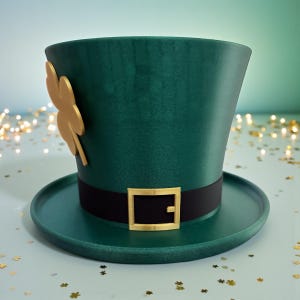 May include: A green leprechaun hat with a black band and gold buckle. A gold shamrock is attached to the side. The hat has a wide brim and a tall, cylindrical crown. The background is a light blue-green.