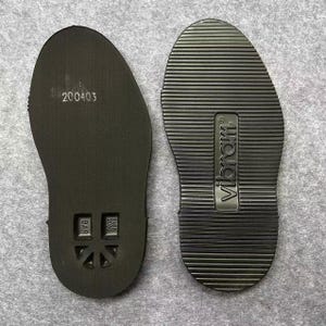 May include: Two black shoe soles. One sole has the number "200403" printed on it, along with other markings. The other sole has the brand name "Vibram" printed on it. Both soles have a textured surface.