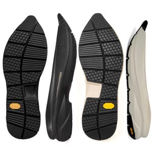 Puede incluir: Dos pares de suelas de zapato con banda de rodadura de goma negra con patrón de estrellas y un logotipo amarillo de Vibram. Un par es completamente negro, mientras que el otro tiene una entresuela beige claro y una punta puntiaguda.