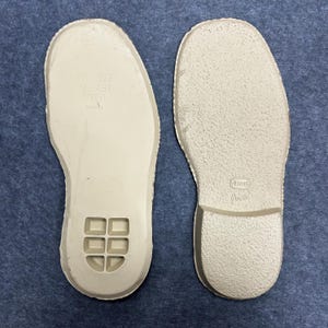 May include: Two off-white shoe insoles. One insole has the text "ART-2302 MS-434 21651". The other insole has the Vibram logo and the word "Quatra". Both insoles have a textured surface and are designed for footwear.