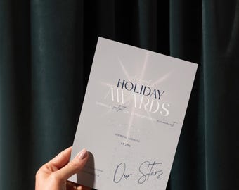 Könnte beinhalten: Eine silberne Einladungskarte mit dem Text "Annual Holiday Awards" und dem Datum "12-20-23". Die Karte wird von einer Hand vor einem dunkelgrünen Vorhang gehalten.