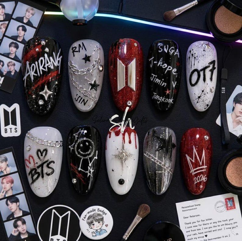 Puede incluir: Un juego de diez u&ntilde;as postizas con varios dise&ntilde;os que incluyen los textos Arirang, RM, Jin, Suga, J-hope, Jimin, V, Jungkook, OT7, BTS y 2026. Las u&ntilde;as est&aacute;n decoradas con cadenas met&aacute;licas, dijes de estrellas, motivos de coronas, caritas y gotas rojas.