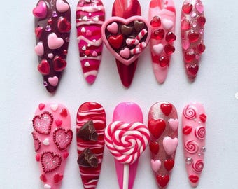Ongles pressés pour la Saint-Valentin avec coeurs, sucette, breloques en chocolat et volutes roses - Ensemble de décorations d'ongles romantiques et sucrées faits main