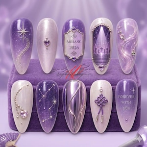 May include: A collection of ten purple and white nail designs. Each nail features unique embellishments, including stars, hearts, and intricate patterns. One nail displays the text "ARIRANG 2026" and another reads "FOREVER WITH YOU".